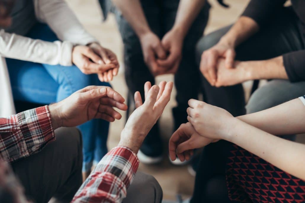 Close-up of hands of people sitting in a circle during a therapy group meeting