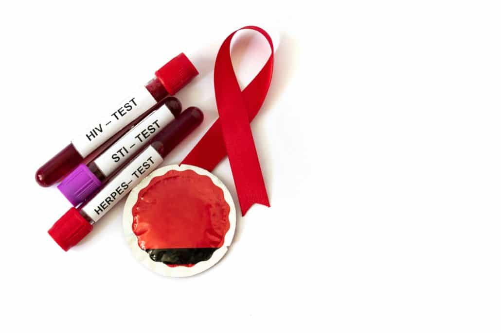 AIDS ribbon with blood tubes from sexually transmitted disease tests and condom on white background